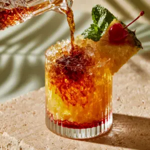 Eye-level smartphone photo of amaretto island punch being poured into a modern ribbed glass with crushed ice. (amaretto island punch)