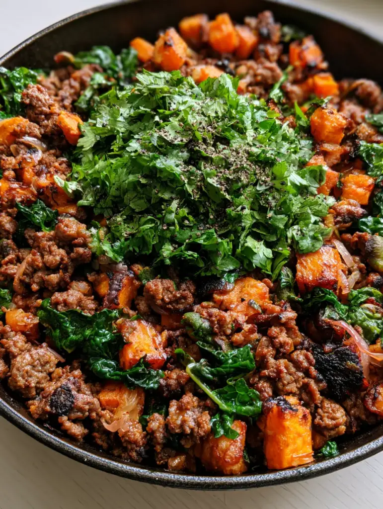 Close up of wilted kale and translucent red onions folded into a ground beef sweet potato bowl.