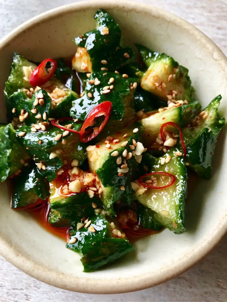 Cucumber Salad Recipe: Spicy Smashed Persian Cucumbers with Chili Oil 2 Macro shot of smashed Persian cucumbers with jagged edges in a glossy red chili oil dressing. (Cucumber Salad Recipe)