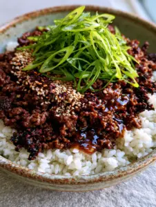 Close-up of deeply browned, crumbly ground beef coated in a thick, glossy amber sauce over white rice. (ground beef bowl recipes)