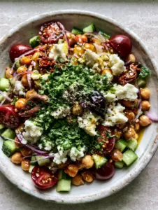Close-up of a greek chickpea salad showing glistening golden dressing on cherry tomatoes and crunchy cucumbers.
