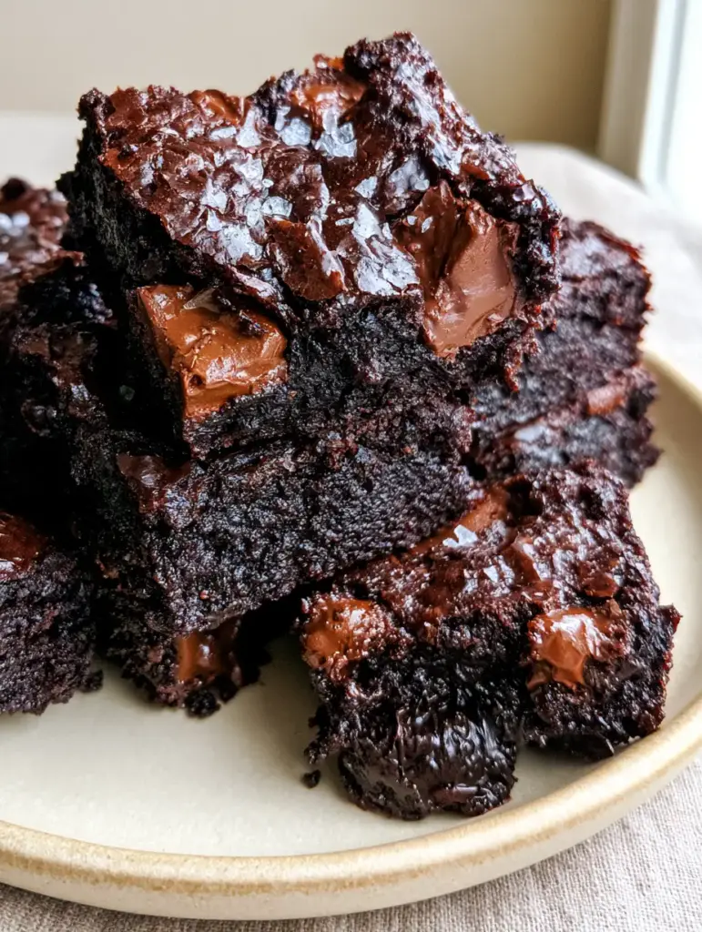 Extreme close-up of a stack of Zucchini Brownies with flaky sea salt garnish and melting chocolate chunks.