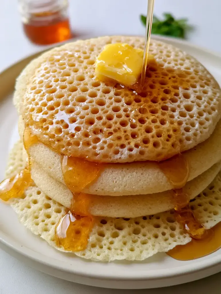 A vertical shot of Moroccan Baghrir African crepes with a thick amber honey-butter mixture filling the tiny holes.